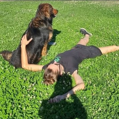 Une femme allongée dans l'herbe, bras ouverts, avec un grand chien assis contre elle